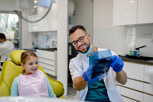 In a well-equipped dentist's office, a child undergoes a thorough dental examination, with the dentist using x-ray equipment to ensure comprehensive care and hygiene