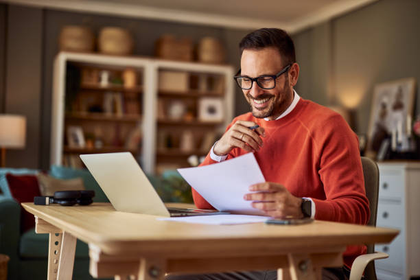 istock A smiling male remote worker comparing a document in his hand to the one on his laptop. 1927152015