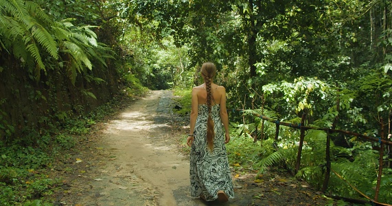 Young woman walking along forest path in jungle. Girl goes down to isolated beach accessed through dense forest with natural swimming pools. Tembeling, tourist attraction in Indonesia. Nusa Penida Bali.