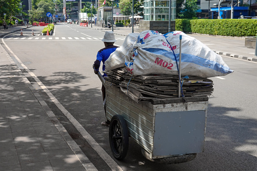 Jakarta, indonesia - desember 17, 2022: Scavengers in the city are carrying their cart filled with piles of used cardboard.