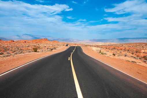 An image showcasing a road stretching through the Arizona desert, cutting a solitary path across the vast, arid landscape. The scene captures the stark beauty of the desert with its rugged terrain and endless horizons under the clear blue sky, embodying the spirit of adventure and the allure of the open road.