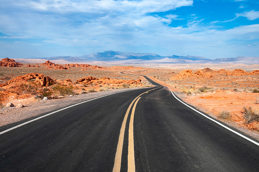 An image showcasing a road stretching through the Arizona desert, cutting a solitary path across the vast, arid landscape. The scene captures the stark beauty of the desert with its rugged terrain and endless horizons under the clear blue sky, embodying the spirit of adventure and the allure of the open road.