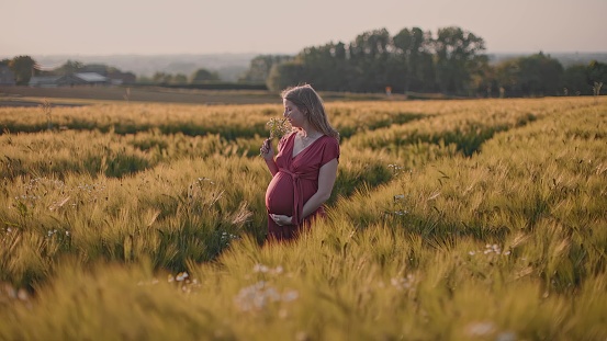 Pregnant woman smelling a bouquet of flowers in the middle of a field at sunset