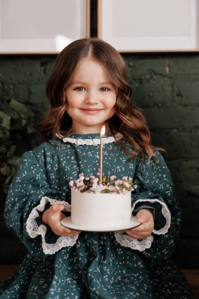 adorable little child girl 4-5 years hold white birthday cake decorated with flowers and trying to blow burning candle. kid wears festive stylish retro dress is ready to her birthday party at home - cute 4 5 years little girls party 뉴스 사진 이미지