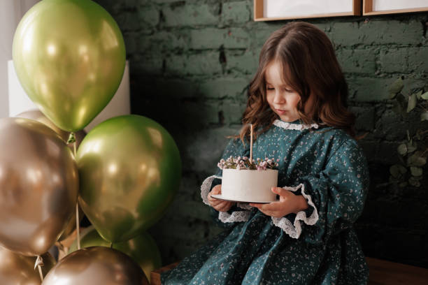 adorable little child girl 4-5 years hold white birthday cake decorated with flowers and trying to blow burning candle. kid wears festive stylish retro dress is ready to her birthday party at home - child caucasian little girls 3 4 years photos et images de collection