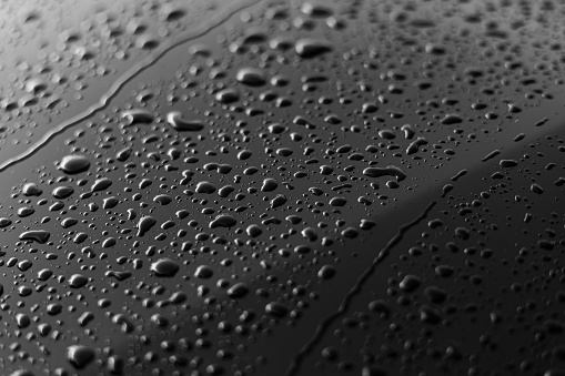 Rain or water drops different size on a black shiny car hood surface. Water droplets on dark iron surface and texture. Abstract background and water texture for design