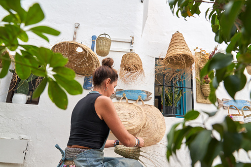 Side view of Hispanic woman weaving a cesco with esparto fibers. Manual work, tradition and culture.