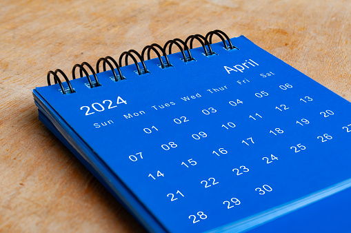 April 2024 blue table calendar on wooden desk. Month concept.