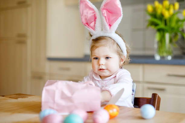 cute little toddler girl wearing easter bunny ears playing with colored pastel eggs. happy baby child unpacking gifts. adorable healthy smiling kid in pink clothes enjoying family holiday - bunny girl stock-fotos und bilder