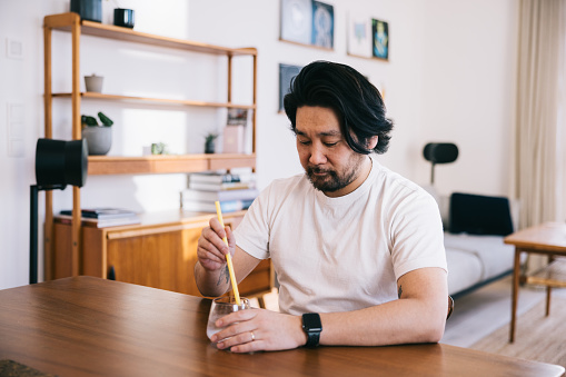 Dentin hypersensitivity. Japanese man in his forties uses a straw to drink water, showcasing a considerate way to bypass tooth sensitivity and enjoy a refreshing beverage