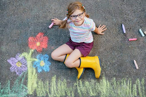 Cute little girl and flowers painted with colorful chalks on asphalt. Happy preschool child having fun with painting chalk picture. Creative leisure for children, drawing and painting