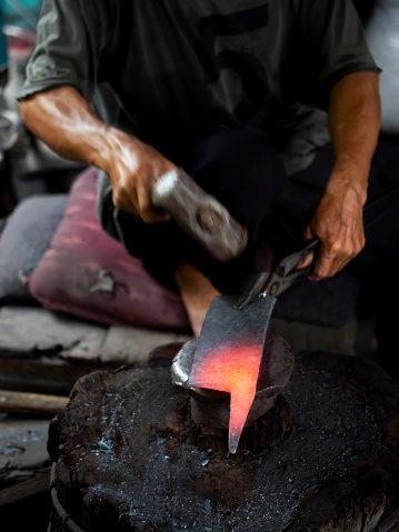 An unrecognizable blacksmith forges hot metal with a hammer on an anvile.