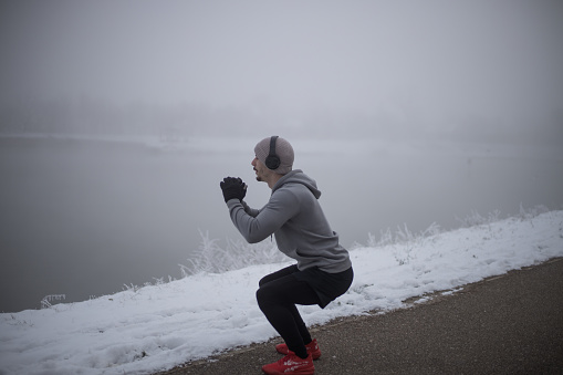 a young man doing squats by the lake