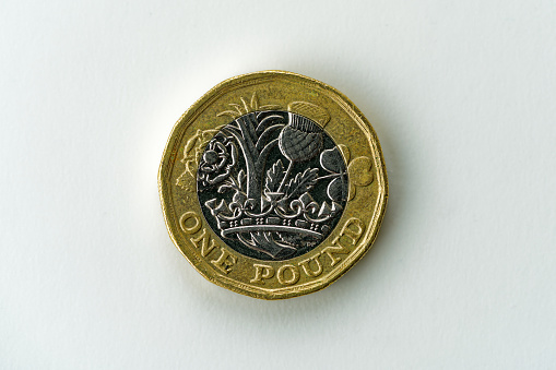 Top close-up view of silver and gold colored British one Pound coin with thistle and clover leaf against white background. Photo taken January 12th, 2024, Zurich, Switzerland.