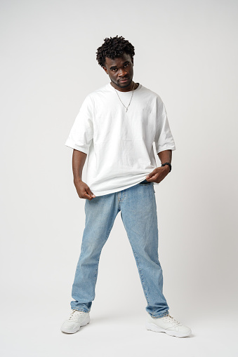 Portrait of a smiling young african man wearing white t-shirt standing over gray background in studio