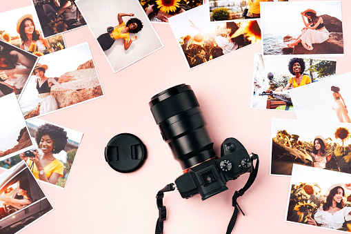 Modern photo camera with printed colorful photos on pink background close up