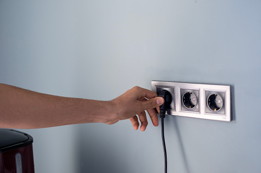 Hand of young man plugging cable into electrical outlet