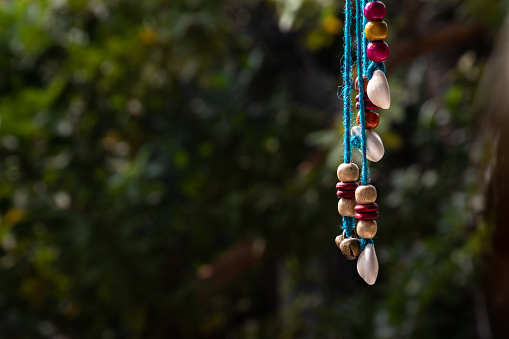 This is a close up vie of stringed wooden beads and shells in the blurred background of dense foliage.