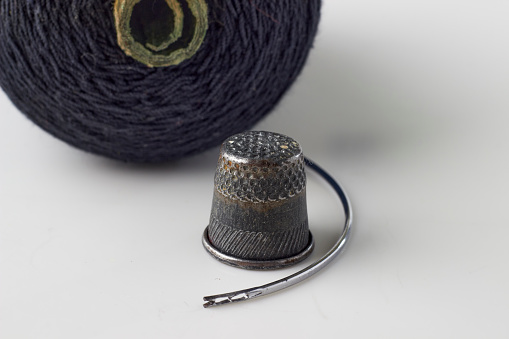Metal thimble, sewing needle and spool of black thread on a white background.