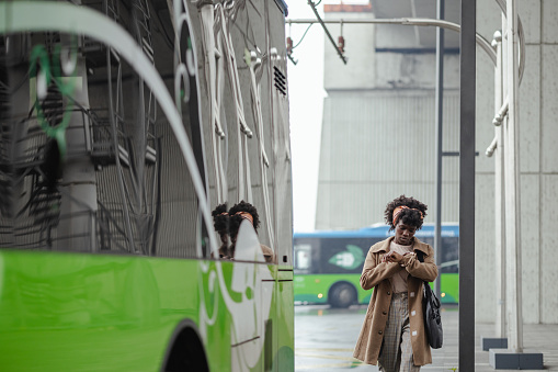 Shot of young African American woman rushing to the bus and checking time