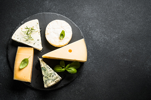 Cheese platter with craft cheese assortment on slate board at black background. Top view with copy space.