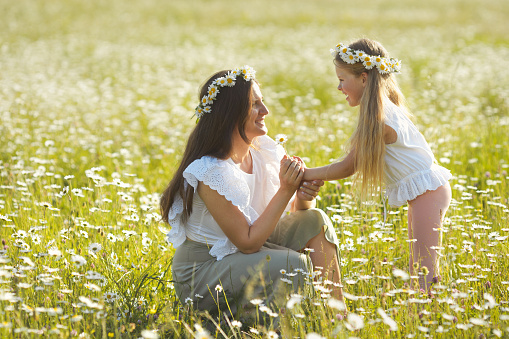 Lifestyle mother and little child in cotton casual clothes playing together in chamomile field. Mom and daughter walking in nature countryside in spring day.
