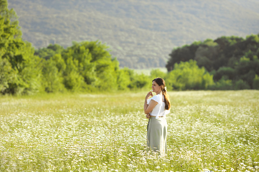 Alone yound dreaming woman walking in chamomile blooming field. Copy space. Ecotherapy and nature therapy concept.