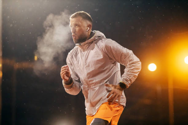 An urban runner is running on city street on snowy cold weather at night. A city runner is running on an urban street on cold rainy weather at night. night runners stock pictures, royalty-free photos & images