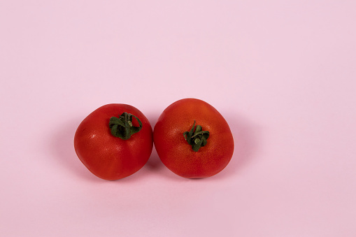 Two fresh tomatoes on a pink background
