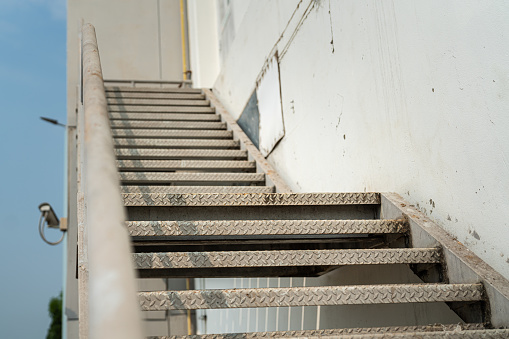 The metal with banister stair walkway outside a factory building, using as emergency exit or service route. Close-up and selective focus on handrail part.