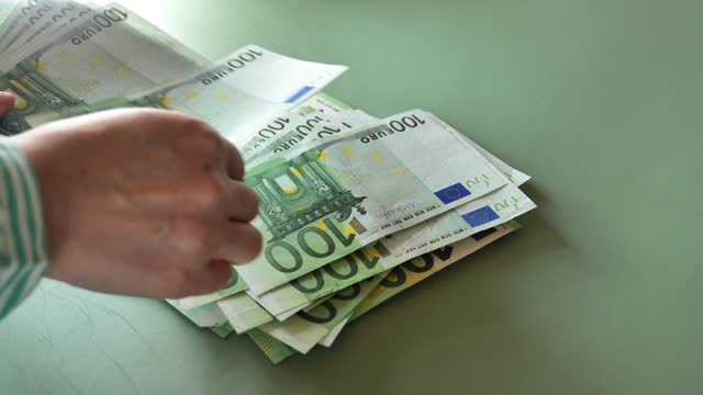 100 euro banknotes on a green background.Hands counting  euro banknotes.European Union money.Earnings and spending in the Eurozone.