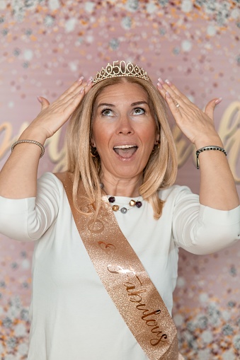 Cheerful blond woman in a white t-shirt, wearing a crown with number 50 having fun in a studio with Happy Birthday background.