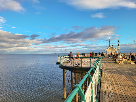 Penarth, Wales, UK: January 06, 2024: Men fish from Penarth Pier in January. A sunny winters day leisure activity. Tourists enjoy the views from the pier.
