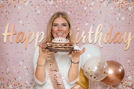 Adult blond woman holding a cake with a crownwith number 50 on it and smiling.