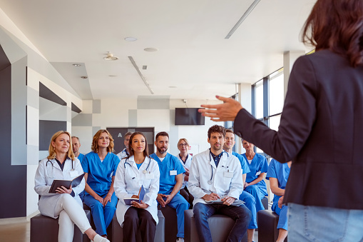 Group of female and male doctors and nurses attending medical seminar. Rear view of speaker talking to smiling healthcare workers sitting in a conference hall.