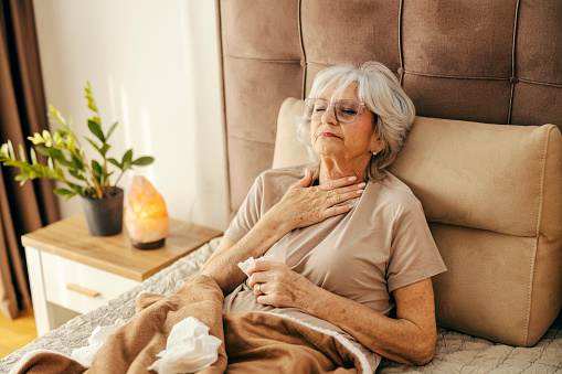 An ill senior woman with sore throat is lying in bed and feeling unwell.