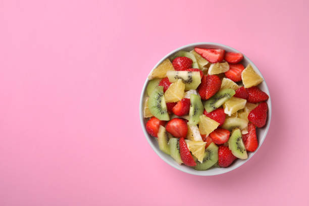 istock Yummy fruit salad in bowl on pink background, top view. Space for text 1927611250