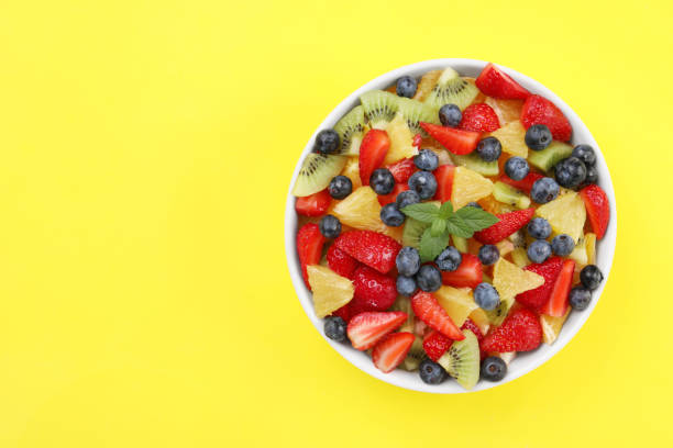 istock Yummy fruit salad in bowl on yellow background, top view. Space for text 1927613937
