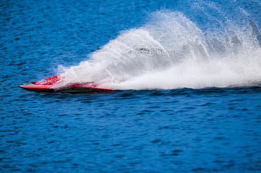 RC racing boat on straightaway skips across the water leaving behind huge spray and ripples.