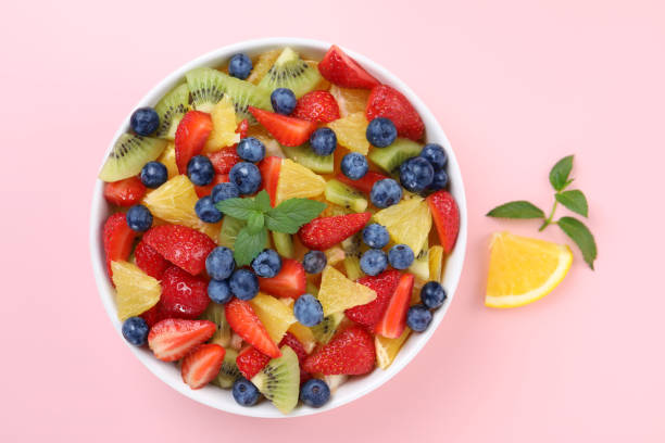 istock Yummy fruit salad in bowl on pink background, top view 1927614977