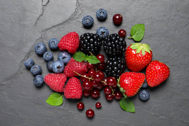 istock Many different fresh ripe berries and green leaves on dark grey table, flat lay 1927614979