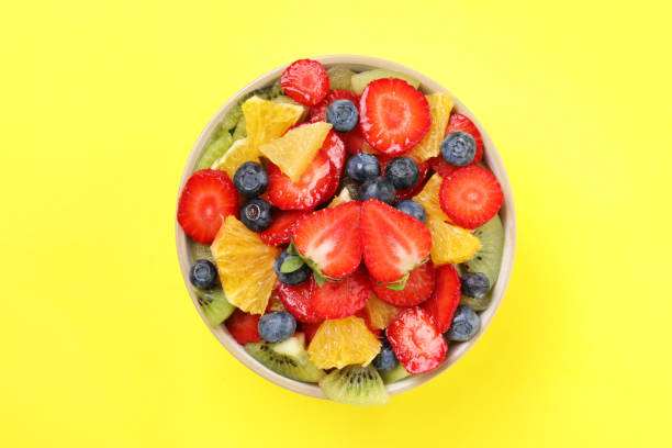 istock Yummy fruit salad in bowl on yellow background, top view 1927615662