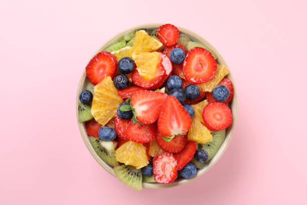 istock Yummy fruit salad in bowl on pink background, top view 1927616098