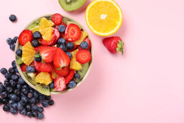 istock Yummy fruit salad in bowl and ingredients on pink background, flat lay. Space for text 1927616109