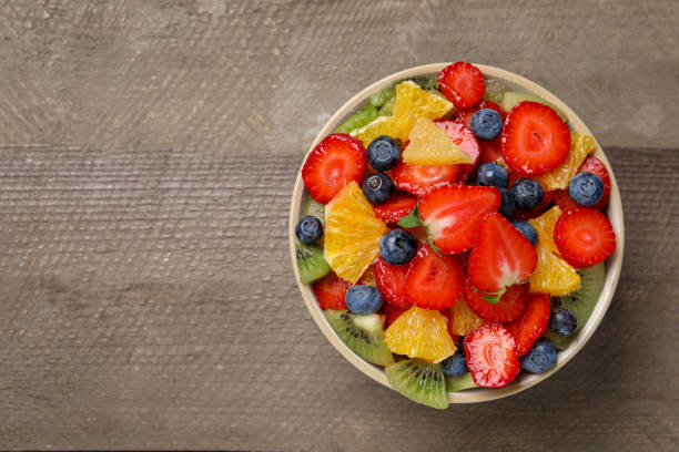 istock Delicious fresh fruit salad in bowl on wooden table, top view. Space for text 1927616614