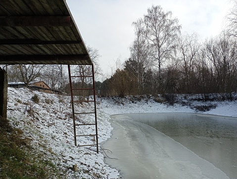 The platform from which the doabina descends to a frozen small pond with a low water level. Winter rest in nature near the pond.