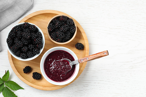 Fresh ripe blackberries and tasty jam on white wooden table, flat lay. Space for text