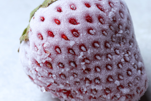 One frozen ripe strawberry on light table, closeup