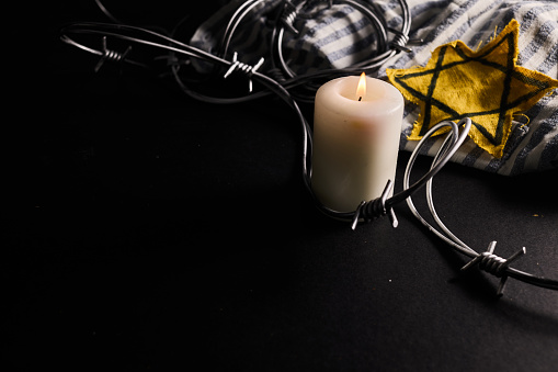 Holocaust memory day. Arbed wire and burning candle on black background.