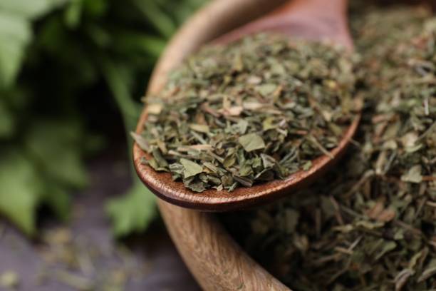 istock Dried aromatic parsley and spoon in bowl on table, closeup 1927648646